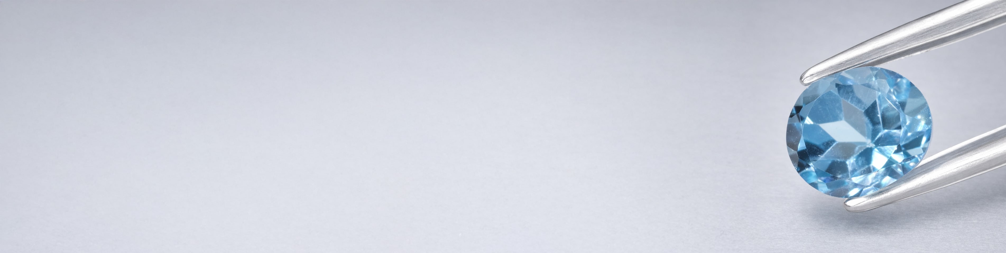 Niebieski topaz w szczypcach jubilerskich na szarym tle